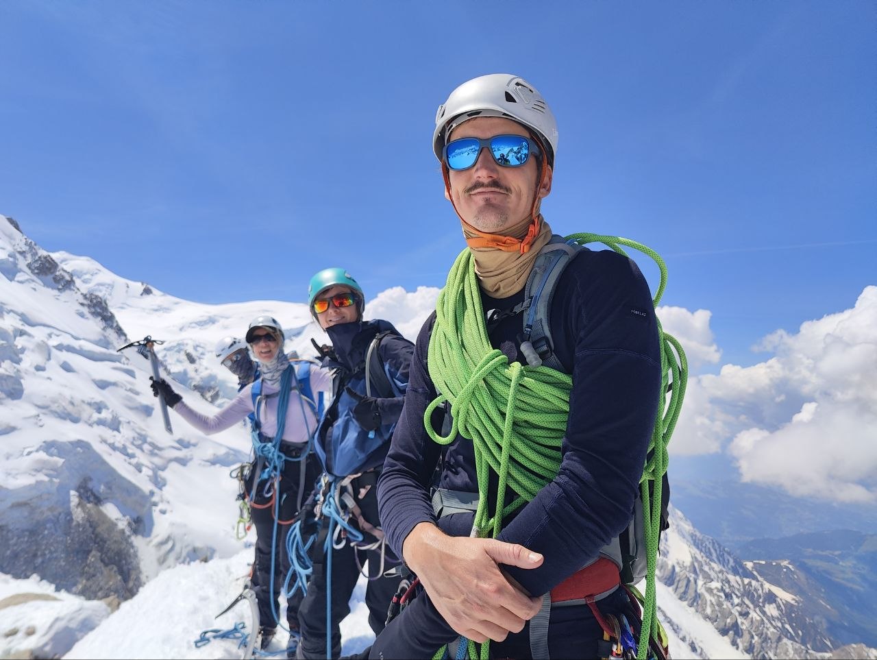 Olivier en tête de cordée avec son équipe au sommet d'une arête enneigée, corde à l'épaule.